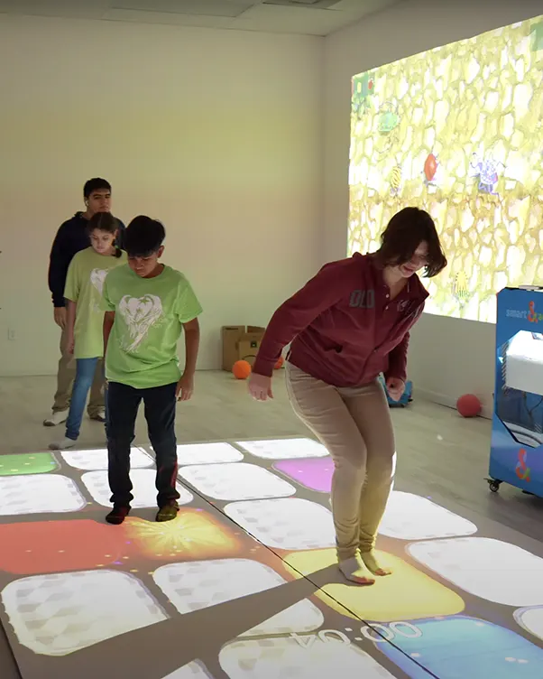 Kids and adult playing on interactive colorful LED floor tiles with wall projection