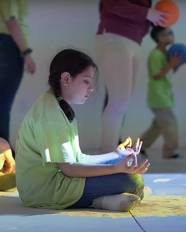 Girl in green shirt meditating cross-legged on interactive floor