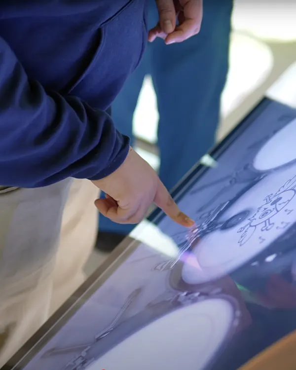 Child pointing at interactive touchscreen with cartoon drawings