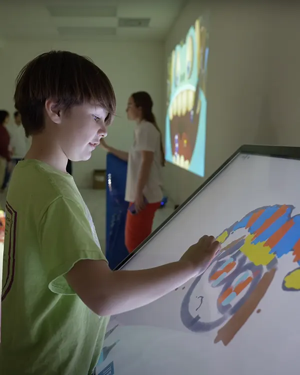 Boy in green shirt drawing on interactive digital whiteboard