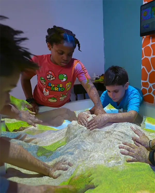 Children interacting with interactive sand table showing projected landscape