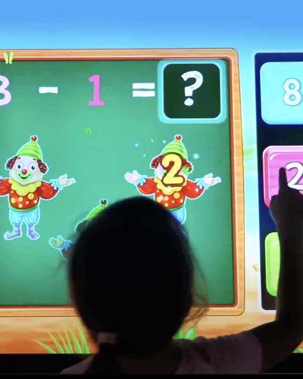 Child pointing at interactive screen solving math problem with cartoon clowns